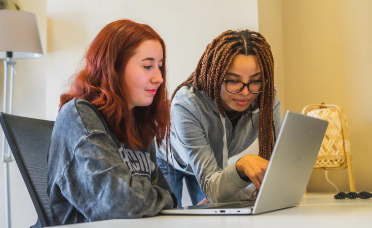 Twee meisjes met lang haar achter een laptop